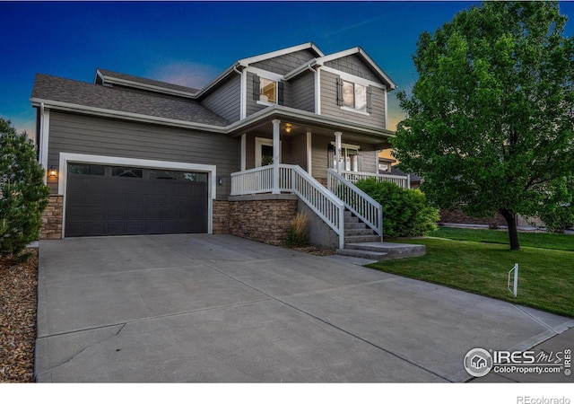 672 Dakota Way, Windsor, CO 80550 - view of front facade featuring covered porch, driveway, a front lawn, an attached garage, and stone siding