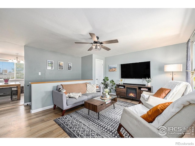 living room featuring baseboards, ceiling fan with notable chandelier, and wood finished floors
