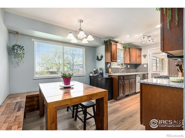 kitchen featuring dishwasher, light countertops, light wood finished floors, backsplash, and a notable chandelier