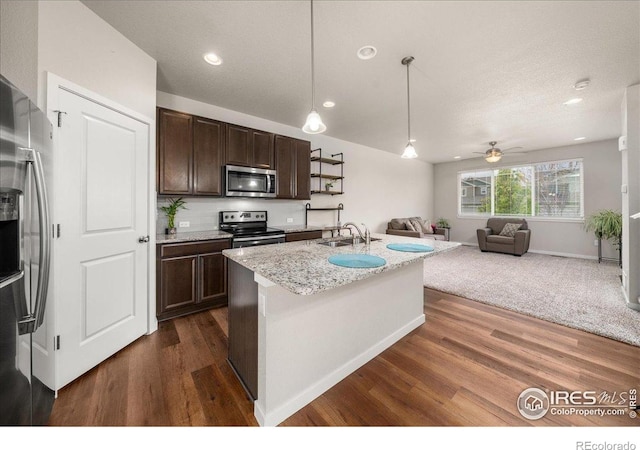 kitchen featuring appliances with stainless steel finishes, dark brown cabinets, a sink, open floor plan, and dark wood-type flooring