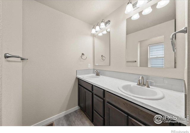 bathroom with a sink, baseboards, double vanity, and wood finished floors