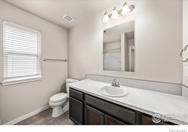 bathroom featuring vanity, toilet, baseboards, wood finished floors, and visible vents
