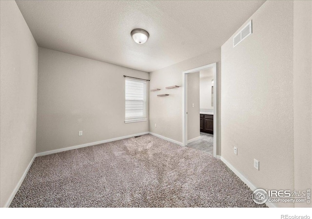 unfurnished bedroom with visible vents, a textured ceiling, carpet floors, and baseboards
