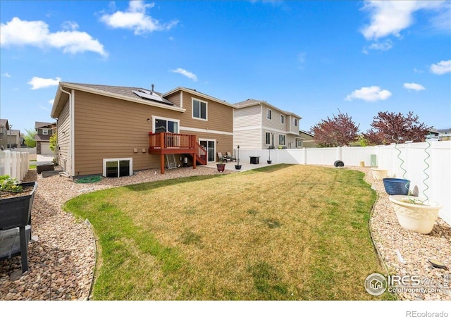 back of property featuring a lawn, a deck, roof mounted solar panels, and a fenced backyard