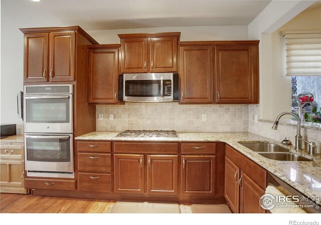 kitchen with decorative backsplash, brown cabinetry, a sink, light stone counters, and stainless steel appliances
