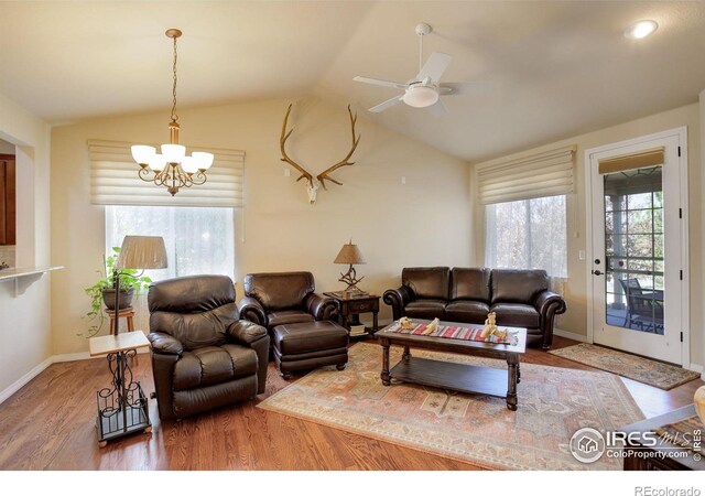 living room with baseboards, ceiling fan with notable chandelier, wood finished floors, and vaulted ceiling