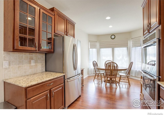kitchen featuring tasteful backsplash, light wood-type flooring, brown cabinets, baseboards, and stainless steel appliances