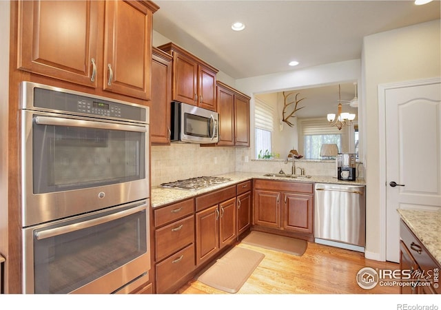 kitchen featuring backsplash, a sink, an inviting chandelier, stainless steel appliances, and light wood-style flooring