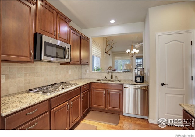 kitchen with appliances with stainless steel finishes, an inviting chandelier, a sink, light wood finished floors, and backsplash