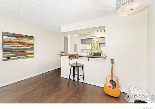 kitchen featuring baseboards, white microwave, a breakfast bar area, and dark wood-style floors