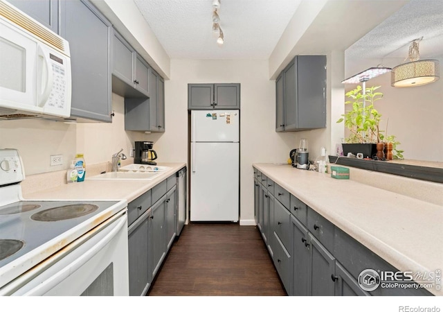 kitchen with a sink, gray cabinets, white appliances, and dark wood-type flooring