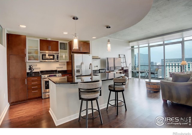 kitchen featuring dark wood-style flooring, dark countertops, appliances with stainless steel finishes, a sink, and a center island with sink