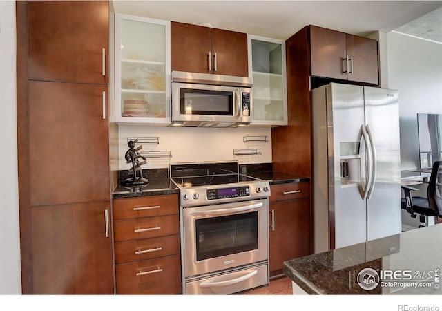 kitchen with stainless steel appliances, glass insert cabinets, and dark stone countertops