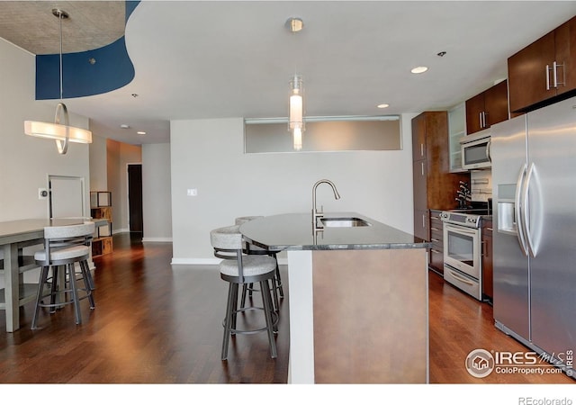 kitchen with a sink, a kitchen breakfast bar, a center island with sink, stainless steel appliances, and dark wood-style floors