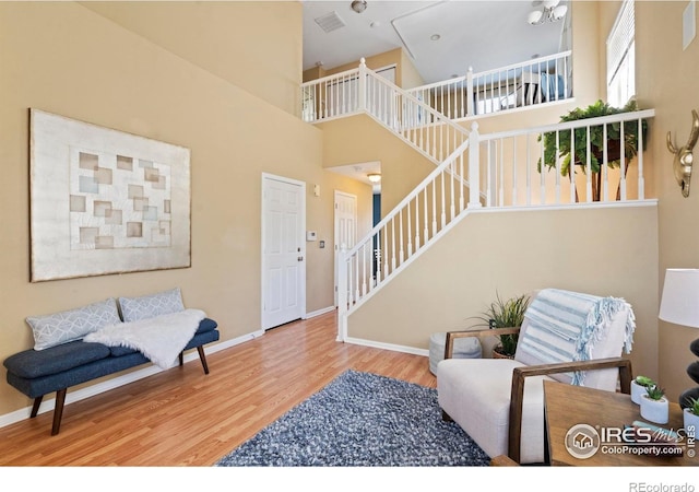 living area featuring visible vents, a towering ceiling, wood finished floors, stairway, and baseboards