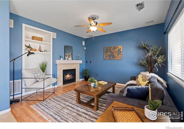 living area with visible vents, wood finished floors, baseboards, ceiling fan, and a tile fireplace