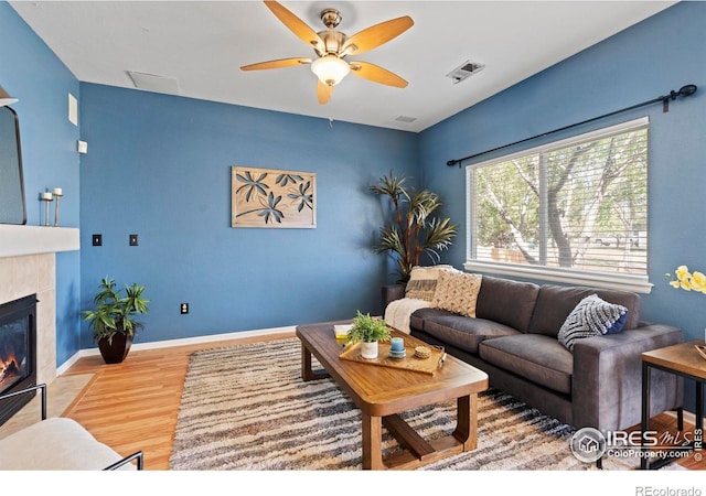 living area featuring a fireplace, a ceiling fan, baseboards, wood finished floors, and visible vents