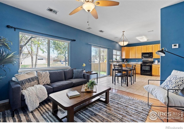 living area featuring light wood-style floors, a ceiling fan, and visible vents