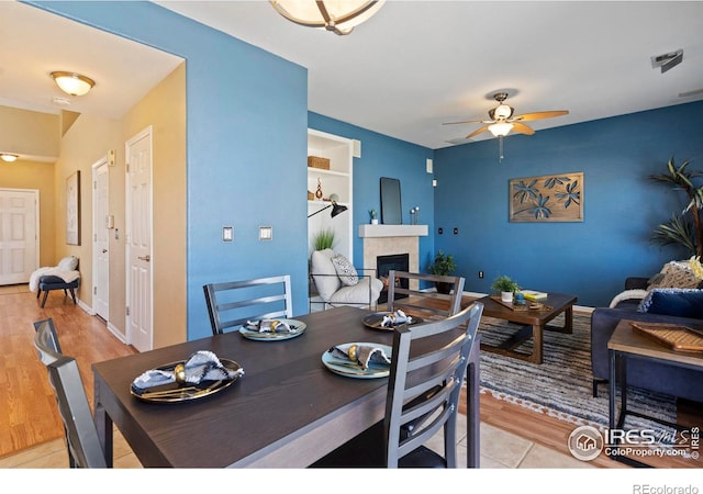 dining room featuring a fireplace, a ceiling fan, and light wood-style flooring