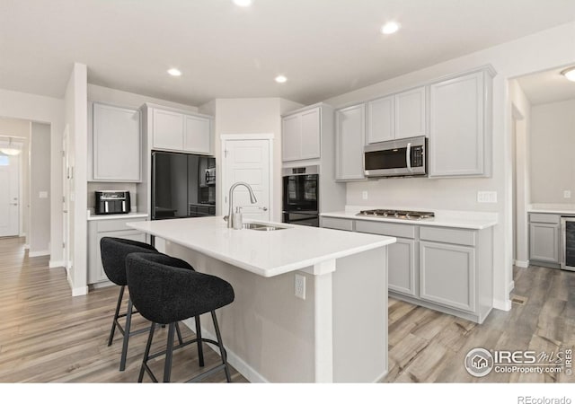 kitchen with a sink, light wood-style flooring, a kitchen breakfast bar, and black appliances