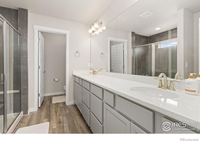 bathroom featuring a sink, double vanity, toilet, wood finished floors, and a stall shower
