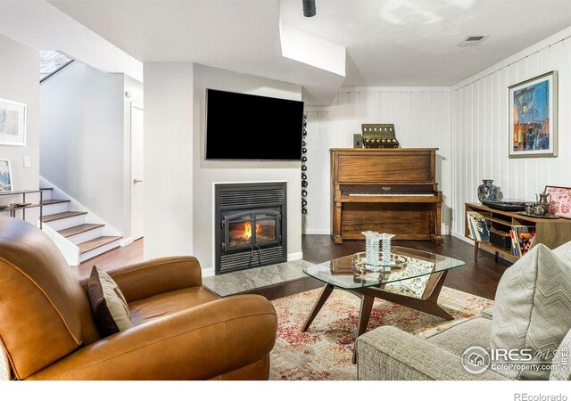 living area featuring a glass covered fireplace, baseboards, wood finished floors, visible vents, and stairway