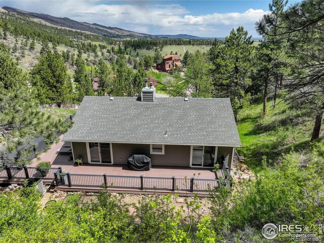 back of house featuring roof with shingles, a deck with mountain view, and a chimney