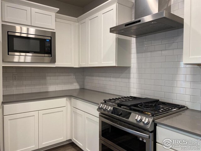 kitchen featuring backsplash, white cabinets, appliances with stainless steel finishes, and wall chimney exhaust hood