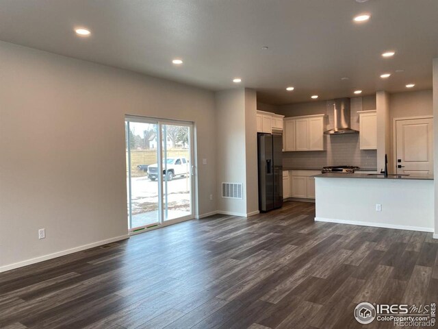 kitchen with wall chimney exhaust hood, open floor plan, dark wood-type flooring, visible vents, and black fridge with ice dispenser