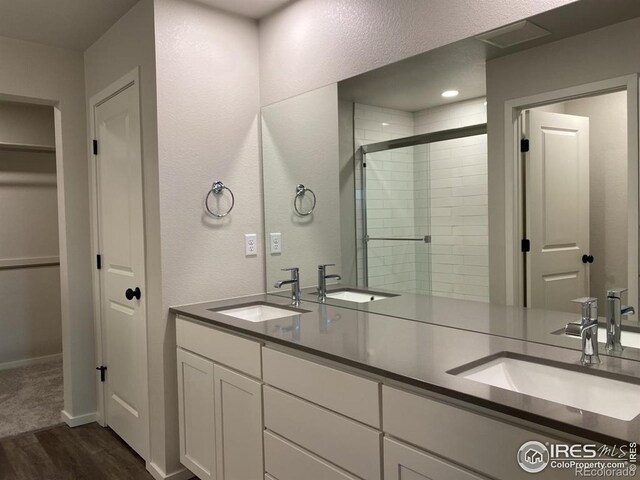 bathroom featuring a sink, double vanity, a stall shower, and wood finished floors