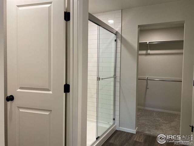 bathroom with baseboards, a shower stall, wood finished floors, and a spacious closet
