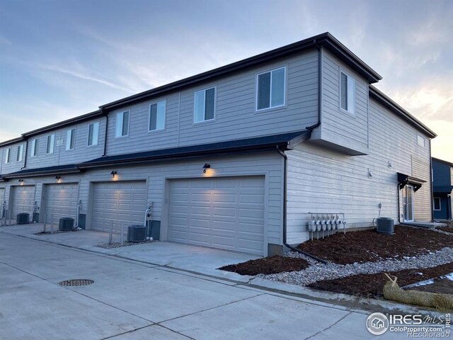 rear view of house with central air condition unit, an attached garage, and concrete driveway