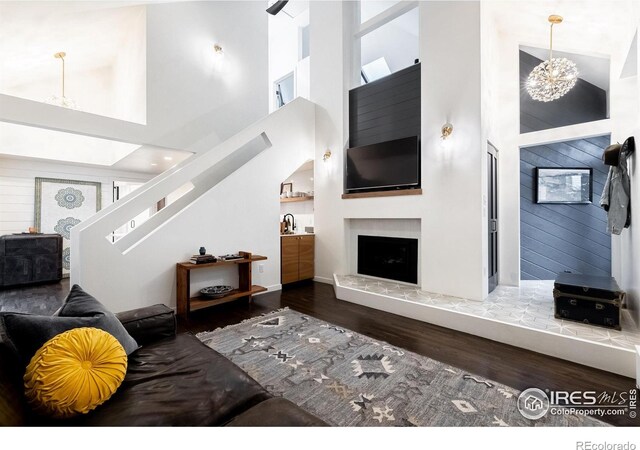 living area featuring a fireplace with raised hearth, a towering ceiling, wood finished floors, and stairway