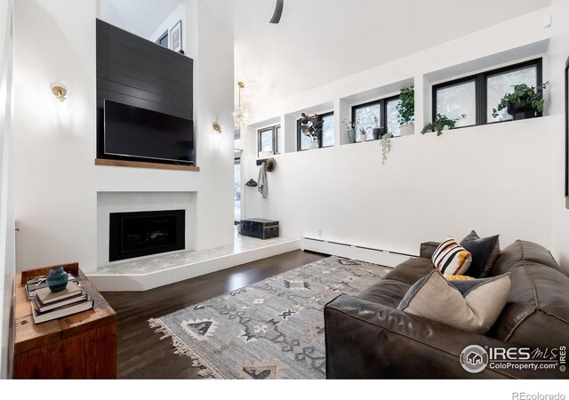 living room with a fireplace with raised hearth, baseboard heating, wood finished floors, and a towering ceiling