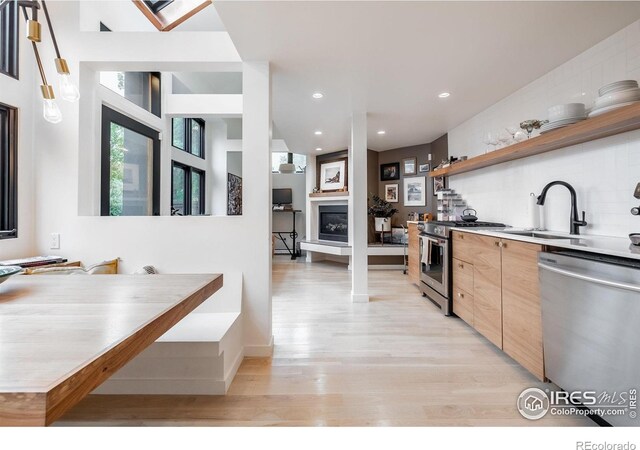kitchen with a sink, a glass covered fireplace, light wood-style flooring, stainless steel appliances, and modern cabinets