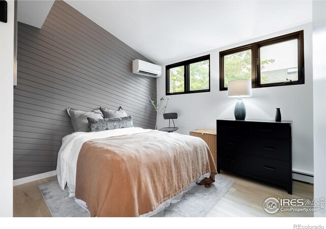 bedroom featuring wooden walls, an AC wall unit, light wood-type flooring, a baseboard radiator, and vaulted ceiling