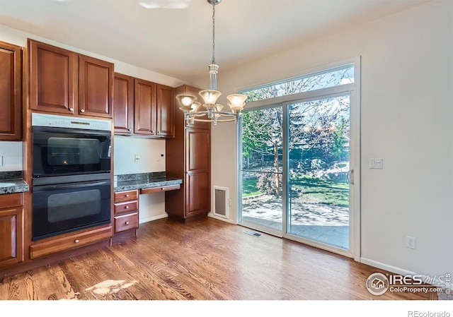 910 Pope Dr, Erie, CO 80516 - kitchen featuring dobule oven black, light wood-style floors, a chandelier, and dark countertops