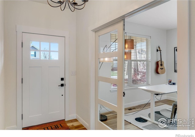 foyer entrance featuring baseboards, wood finished floors, and a notable chandelier