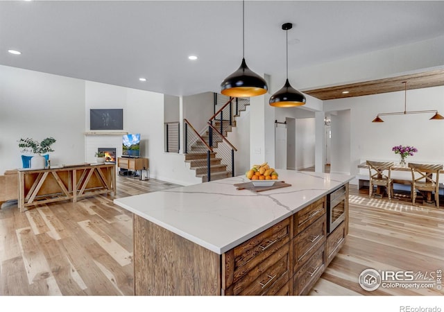 kitchen with a warm lit fireplace, a center island, stainless steel microwave, light stone counters, and light wood-style flooring