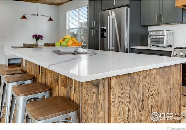 kitchen featuring a breakfast bar area, a large island, light stone countertops, high end refrigerator, and a toaster