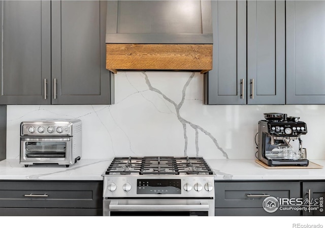 kitchen featuring decorative backsplash, gray cabinets, gas range, light stone counters, and custom exhaust hood