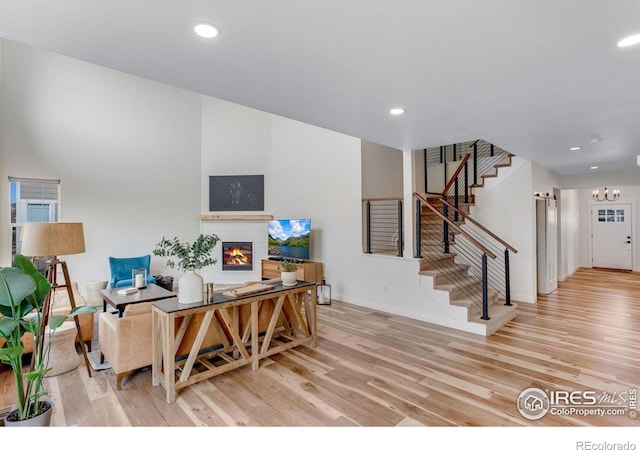 living room featuring light wood-style floors, stairs, a glass covered fireplace, and baseboards