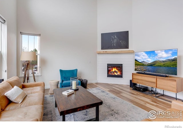 living room featuring a glass covered fireplace, baseboards, a high ceiling, and wood finished floors