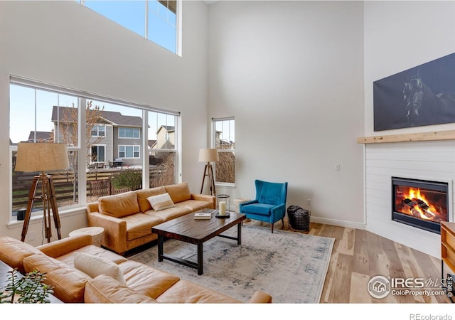living area featuring a glass covered fireplace, baseboards, light wood-type flooring, and a towering ceiling