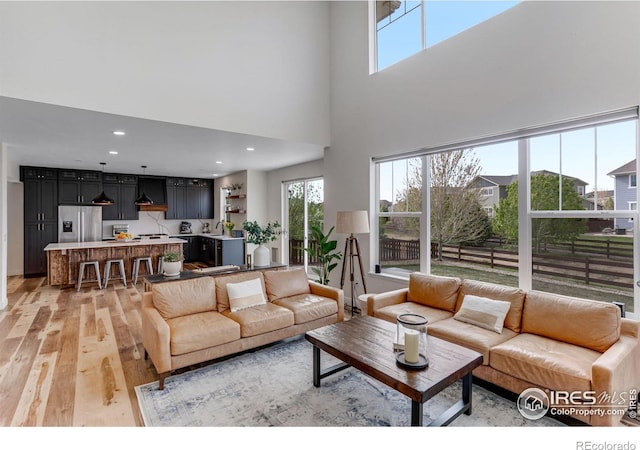 living room with light wood-type flooring, recessed lighting, and a towering ceiling
