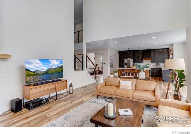 living area featuring stairway, baseboards, a high ceiling, and light wood-style flooring