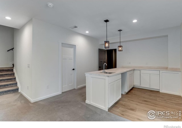 kitchen with pendant lighting, a sink, light countertops, white cabinets, and a peninsula