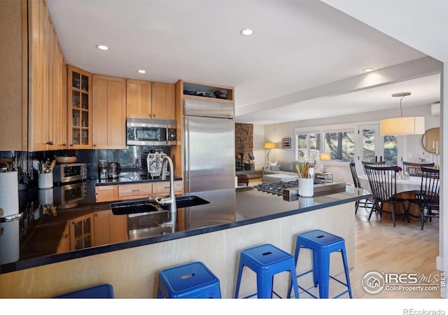 kitchen featuring dark countertops, a breakfast bar area, a sink, appliances with stainless steel finishes, and backsplash