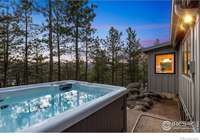 pool at dusk with a hot tub