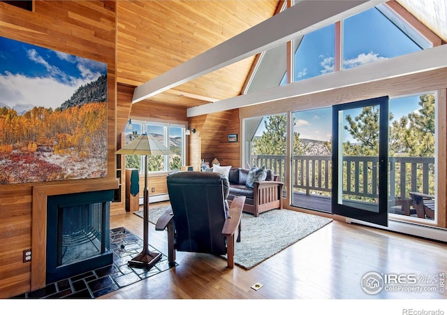 living area featuring wood walls, wood finished floors, high vaulted ceiling, beamed ceiling, and a baseboard heating unit
